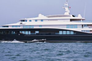 Luxury contemporary private yacht and small motorboat floating in blue ocean against cloudless sky